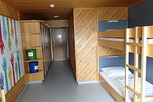 Blick in ein Mehbettzimmer mit zwei Stockbetten und Schränken.