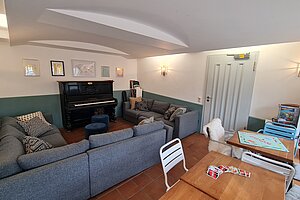 Aufenthaltsraum mit Klavier, um das Sofas gruppiert sind. Auf der anderen Seite des Zimmers steht ein großer Tisch und ein Regal mit vielen Gesellschaftsspielen. 