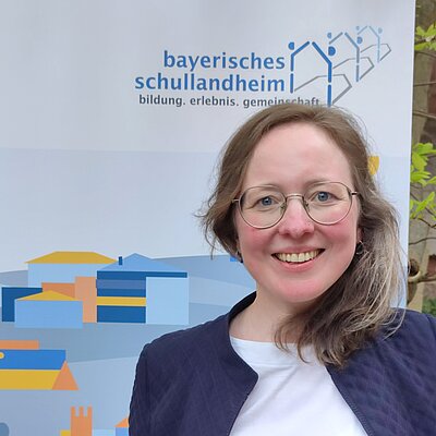 Frau mit Brille vo der Banner "Bayerisches Schullandheimwerk"