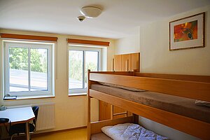 Blick ins Lehrerzimmer mit Hochbett und einem Tisch mit Stuhl.