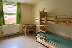 Mehrbettzimmer mit Hochbett und Tisch mit Stühlen in der Ecke.