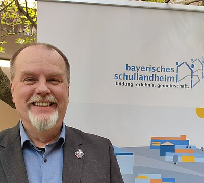 Mann mit Bart vor Banner Bayerisches Schullandheimwerk