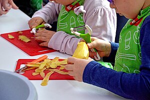 Zwei Kinder mit grüner Schürze schälen Kartoffeln