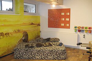 Zimmer mit Sofa mit Streifenfell, Wandild von Savanne mit Löwe und Elefanten.
