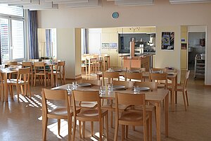 Speisesaal mit Tischen wie Inseln gruppiert. Im Hintergrund das Fenster der Essensausgabe. 
