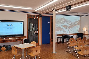 Das Klassenzimmer ist mit einem großen Bildschirm und einem Beamer ausgestattet. 