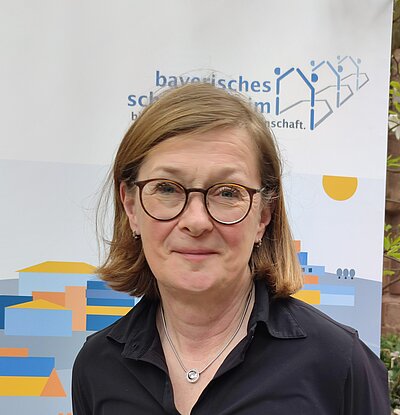 Frau mit Brille und halblangen Haaren vor Banner Bayerisches Schullandheimwerk