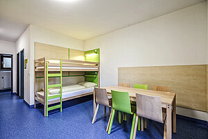 Blick in ein Mehrbettzimmer mit Stockbetten, Tisch und Stühlen. 