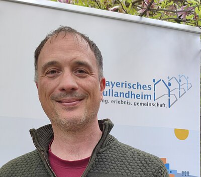 Mann mit grüner Jacke vor Banner Bayerisches Schullandheimwerk