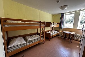 Blick in ein Mehrbettzimmer mit zwei Stockbetten, die hintereinander an der Wand stehen. Gegenüber befinden sich Schränke.