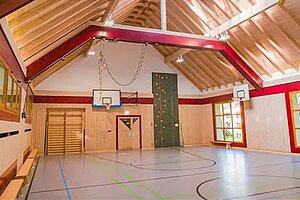 Die Turnhalle des Schullandheims Hobbach hat eine kleine Kletterwand. Die großen Fenster sorgen für einen hellen Raum. 