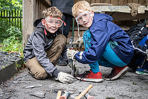 Zwei Schüler sitzen am Boden und bohren Löcher in einen Basaltstein.