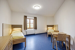 Ein Lehrerzimmer mit Bett, Tisch und Stuhl.