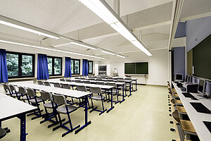 Blick in ein Klassenzimmer, in dem die Tische zum Pult und zur Tafel ausgerichtet sind. 