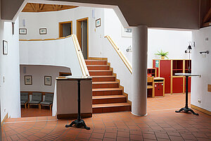 Foyer mit Treppe, Fliesenboden und Stehtischen
