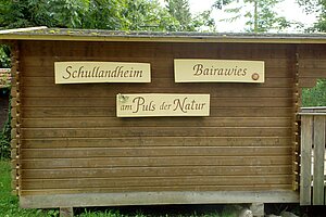 Eine Hüttenwand, auf der das Motto des Schullandheims Bairawies steht: Am Puls der Natur.