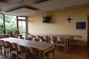 Speisesaal mit langen Tischen und Holzstühlen.