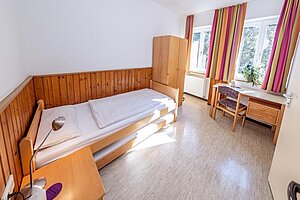 Einzelzimmer für eine Lehrkraft oder Betreuungsperson. Ausgestattet ist das Zimmer mit Bett, Nachtschränkchen, Schrank und Tisch mit Stuhl. 