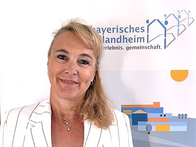 Blonde Frau vor Banner Bayerisches Schullandheim