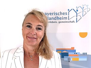 Blonde Frau vor Banner Bayerisches Schullandheim