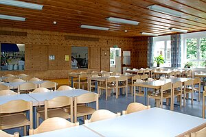 Im Speisesaal stehen die Tisch in Reihen nebeneinander. Im Hintergrund sieht man die Essensausgabe.