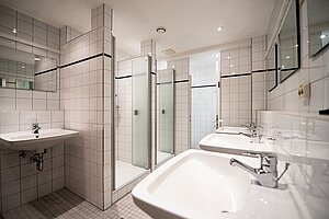 Blick in ein Badezimmer mit mehreren Waschbecken und Duschkabinen.