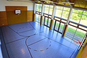 Blick in die Turnhalle, die eine große Fensterfront mit Blick auf die Wiese vor dem Schullandheim. 