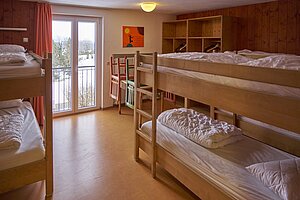 Stockbetten in einem bunt gestrichenen Zimmer, bodentiefes Fenster mit Aussicht.
