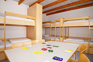 Mehrbetterzimmer mit Stockbetten und Tisch mit Stühlen. Auf dem Tisch liegen Ligrettokarten zum Spielen vorbereitet.